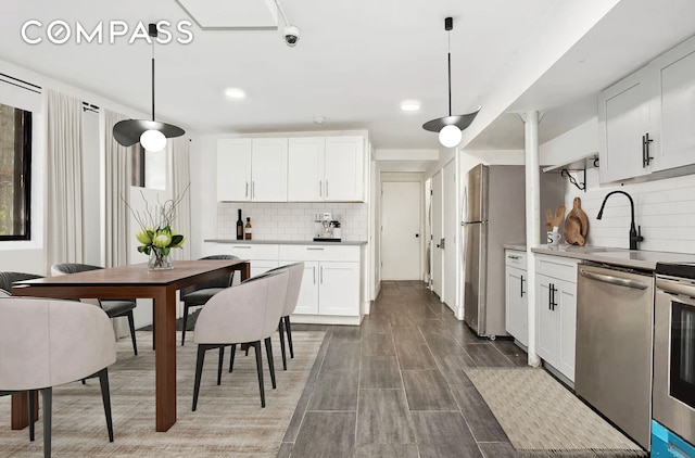 kitchen featuring pendant lighting, decorative backsplash, stainless steel appliances, white cabinetry, and a sink