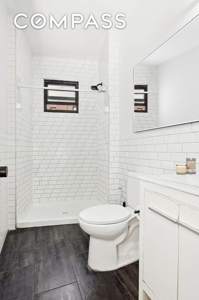 bathroom with a shower stall, tile walls, toilet, wood finished floors, and vanity