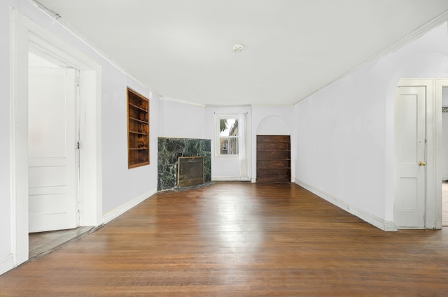 unfurnished living room with a high end fireplace, ornamental molding, baseboards, and wood finished floors