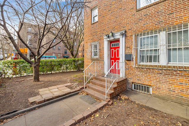 doorway to property featuring brick siding and fence