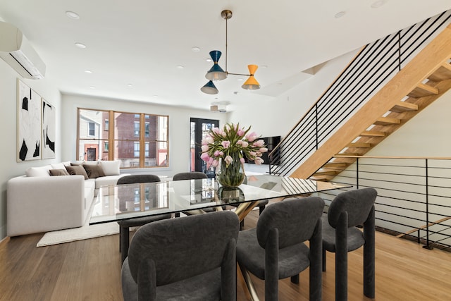 dining space featuring stairs, recessed lighting, an inviting chandelier, wood finished floors, and a wall mounted AC