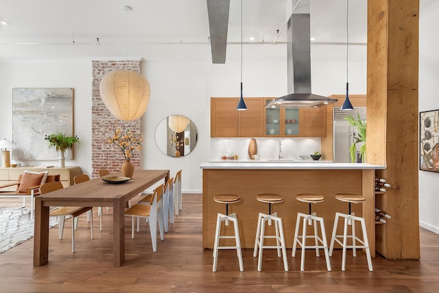 kitchen with brown cabinets, island exhaust hood, a kitchen breakfast bar, wood finished floors, and a towering ceiling