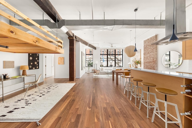 interior space featuring a kitchen bar, open floor plan, wood finished floors, island range hood, and baseboards