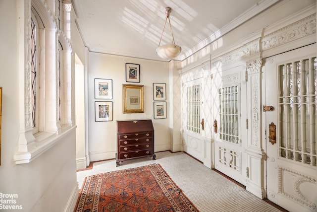 foyer featuring baseboards, crown molding, and ornate columns