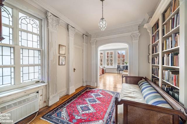 sitting room featuring arched walkways, wood finished floors, crown molding, and radiator heating unit