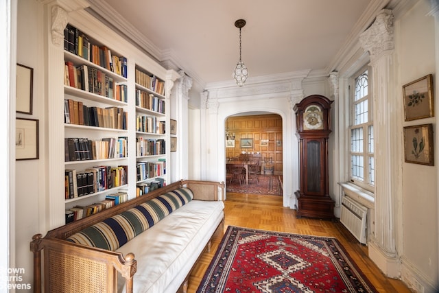 living area with arched walkways, radiator heating unit, and ornamental molding