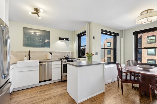 kitchen featuring a sink, a glass covered fireplace, stainless steel appliances, white cabinets, and light wood finished floors