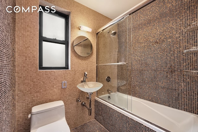 full bath featuring tiled shower / bath combo, toilet, tile walls, and a sink