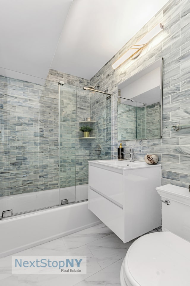 bathroom featuring toilet, marble finish floor, tile walls, enclosed tub / shower combo, and vanity