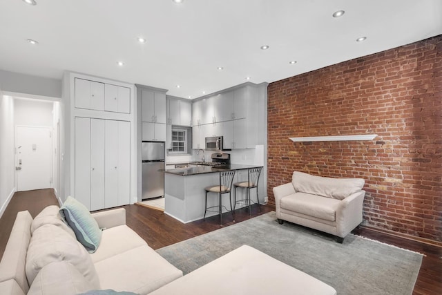 living room with dark wood-style flooring, brick wall, and recessed lighting