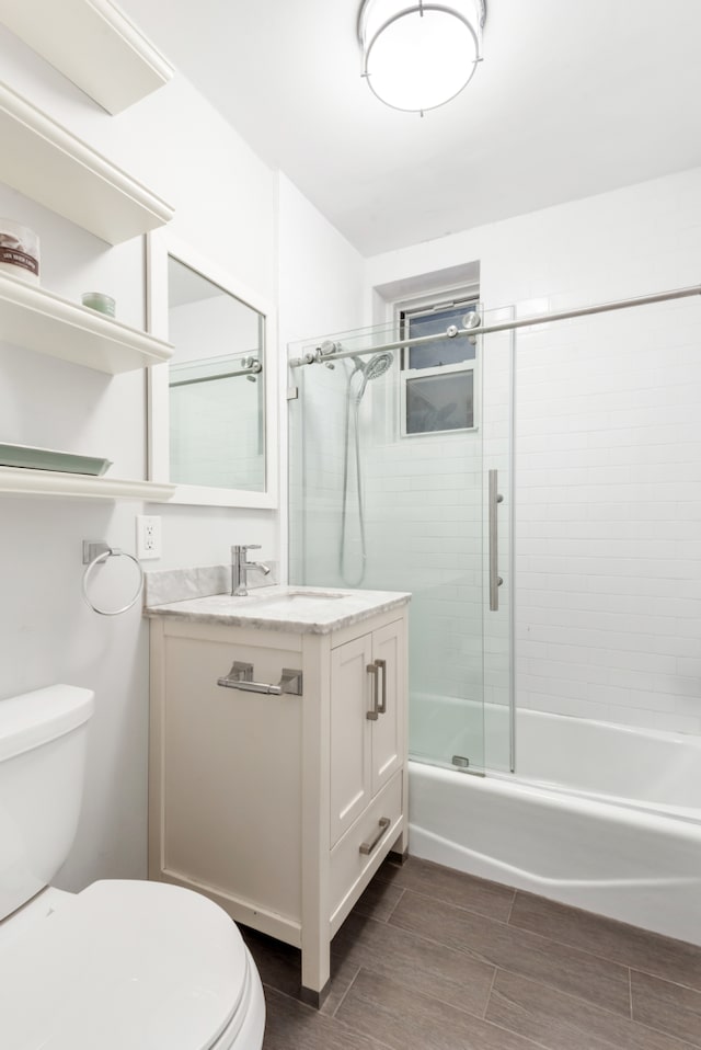 bathroom featuring toilet, wood tiled floors, vanity, and enclosed tub / shower combo