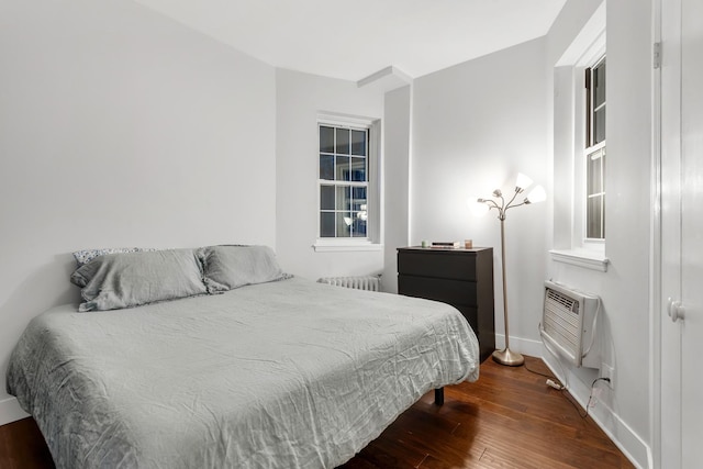 bedroom featuring hardwood / wood-style flooring, baseboards, an AC wall unit, and radiator