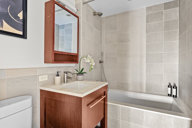 bathroom featuring vanity, tile walls, toilet, and tiled shower / bath