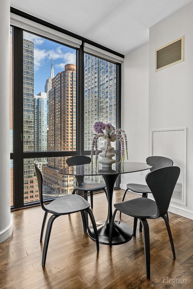 dining space with visible vents, a city view, a wall of windows, and wood finished floors