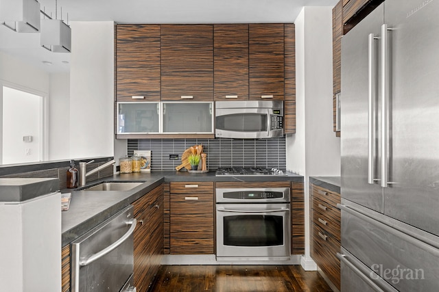 kitchen with dark wood-type flooring, a sink, dark countertops, stainless steel appliances, and decorative backsplash