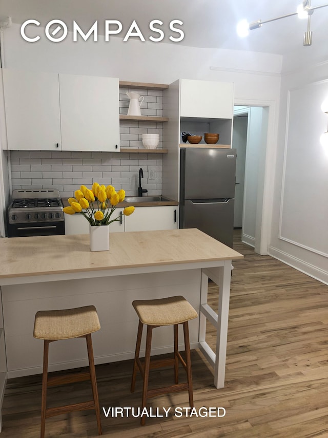 kitchen with freestanding refrigerator, white cabinets, range with gas stovetop, and a sink