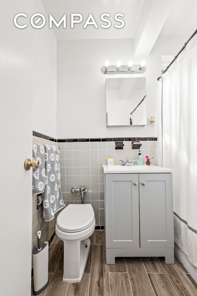 full bath featuring wood finish floors, a wainscoted wall, toilet, and tile walls