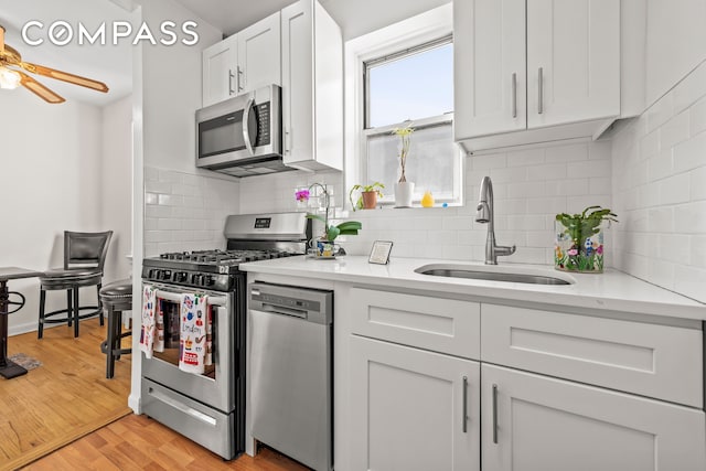 kitchen featuring stainless steel appliances, light wood-style floors, white cabinetry, a ceiling fan, and a sink