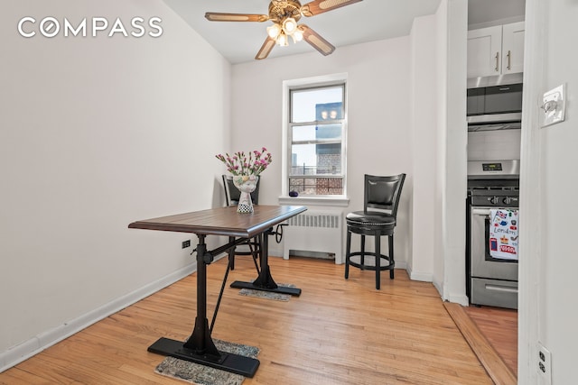 dining room with baseboards, radiator, ceiling fan, and light wood finished floors