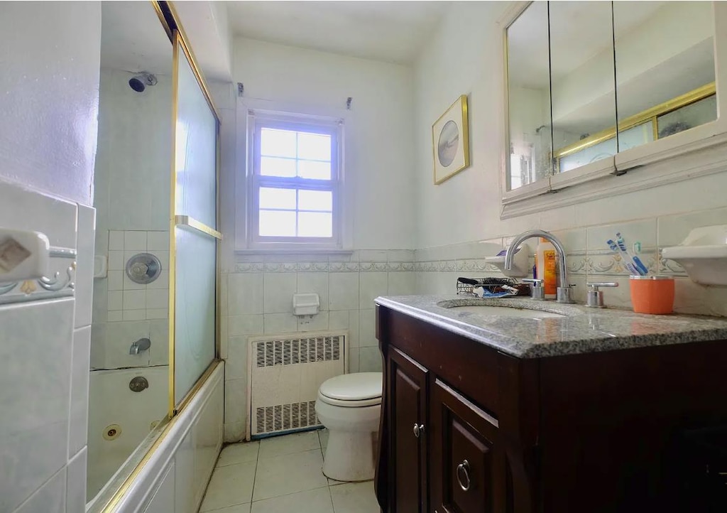 bathroom with toilet, tile walls, radiator, vanity, and tile patterned floors