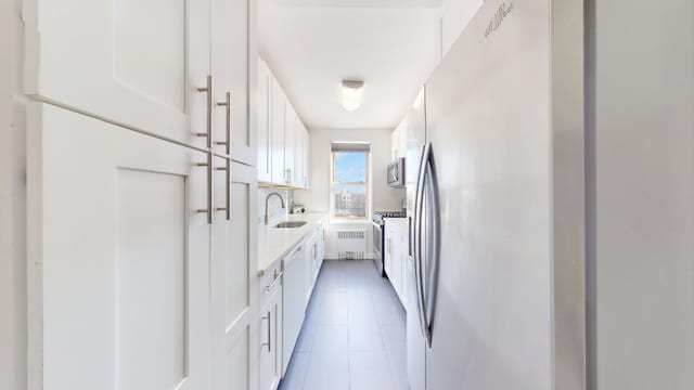 kitchen featuring appliances with stainless steel finishes, a sink, white cabinetry, light countertops, and radiator heating unit