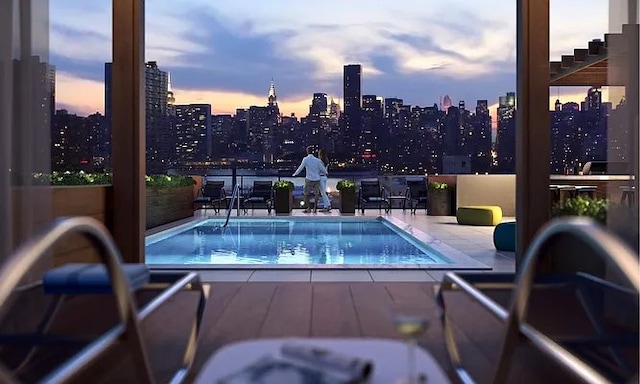 pool at dusk with a patio, a view of city, and a community pool