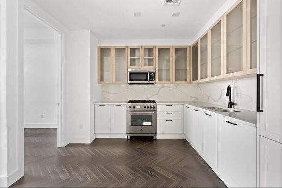 kitchen featuring a sink, stainless steel appliances, glass insert cabinets, and tasteful backsplash