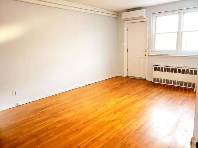 empty room featuring baseboards, wood finished floors, radiator heating unit, and a wall mounted AC