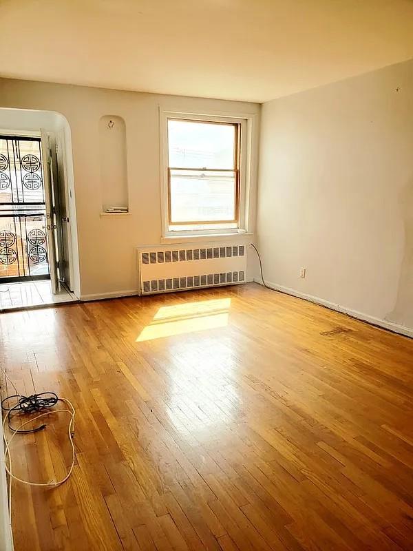 spare room with radiator heating unit, baseboards, and light wood finished floors