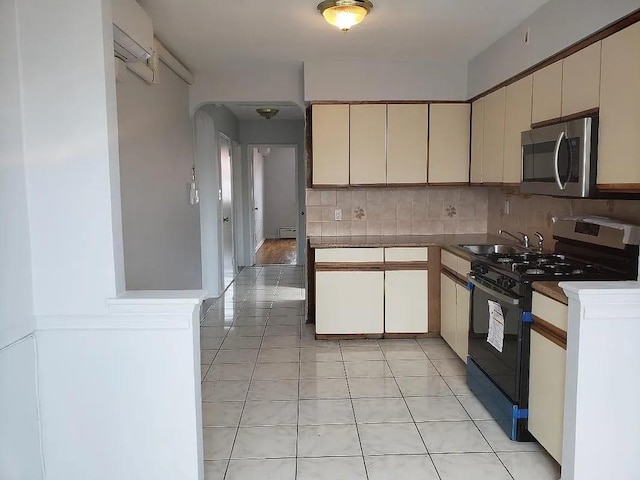 kitchen featuring stainless steel microwave, backsplash, light tile patterned flooring, gas stove, and a sink