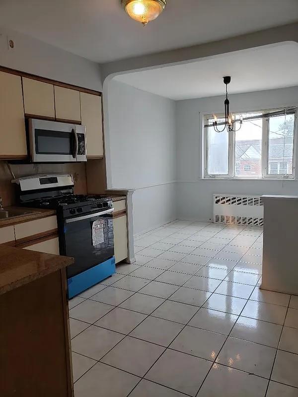 1207 E 83rd St, New York City, NY 11236 - kitchen with stainless steel appliances, radiator, a chandelier, pendant lighting, and light tile patterned flooring