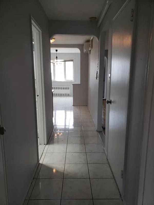 1207 E 83rd St, New York City, NY 11236 - hallway with radiator heating unit, a chandelier, arched walkways, light tile patterned floors, and a wall mounted AC