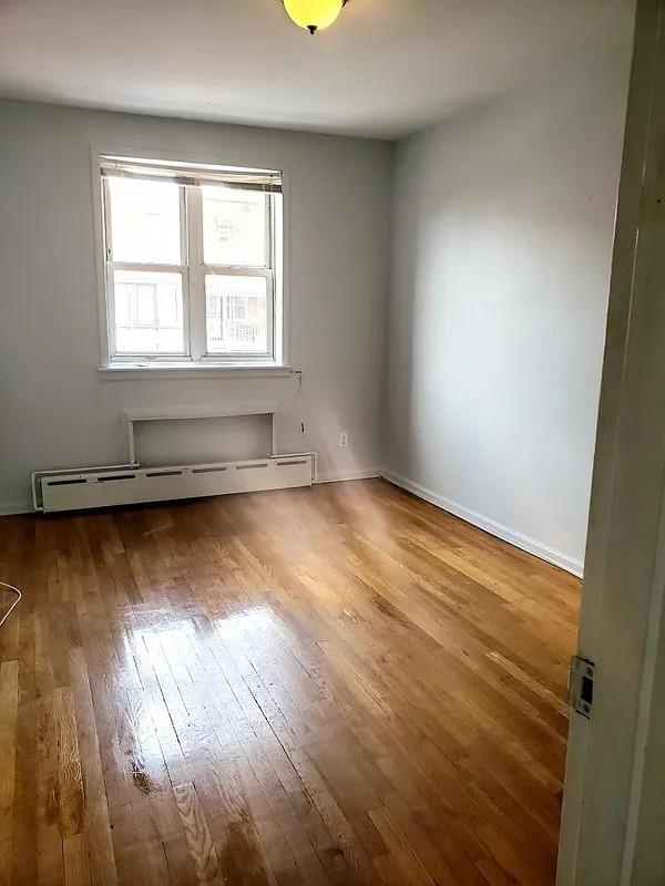 1207 E 83rd St, New York City, NY 11236 - unfurnished room featuring a baseboard heating unit, wood-type flooring, and baseboards
