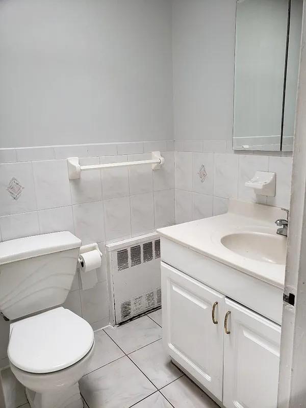 1207 E 83rd St, New York City, NY 11236 - bathroom with radiator heating unit, vanity, toilet, and tile walls