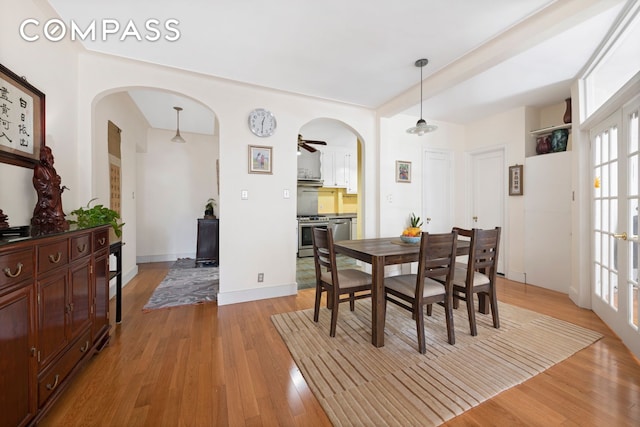 dining room featuring light wood-type flooring, arched walkways, and baseboards