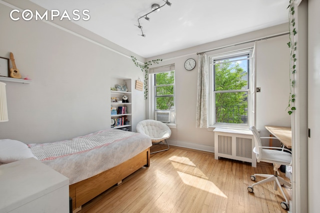 bedroom with cooling unit, baseboards, radiator heating unit, hardwood / wood-style flooring, and track lighting