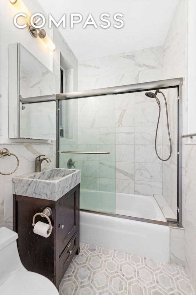 bathroom with vanity, tile walls, toilet, and bath / shower combo with glass door