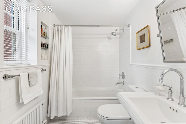 bathroom with radiator, a sink, tiled shower / bath combo, tile walls, and toilet