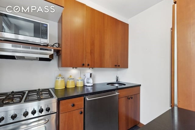 689 Fort Washington Ave Unit 4B, New York City, NY 10040 - kitchen with dark countertops, a sink, brown cabinetry, appliances with stainless steel finishes, and under cabinet range hood