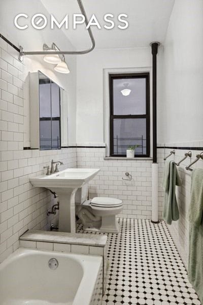 bathroom featuring tile patterned flooring, wainscoting, tile walls, toilet, and a washtub