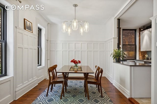 dining area with a decorative wall, a notable chandelier, dark wood-style floors, and wainscoting