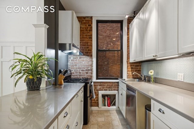 kitchen with brick wall, a sink, white cabinets, appliances with stainless steel finishes, and stone finish flooring