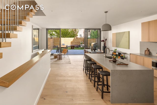 kitchen featuring light brown cabinetry, a kitchen bar, a wall of windows, light wood-type flooring, and modern cabinets