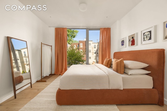 bedroom featuring multiple windows, baseboards, light wood-style floors, and expansive windows