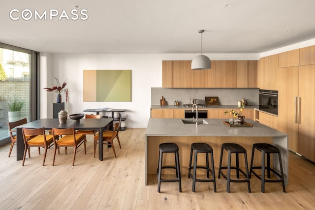 kitchen featuring backsplash, black oven, a kitchen bar, modern cabinets, and a sink