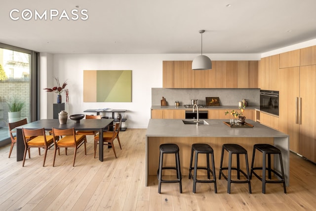 kitchen with oven, modern cabinets, a sink, a kitchen bar, and tasteful backsplash