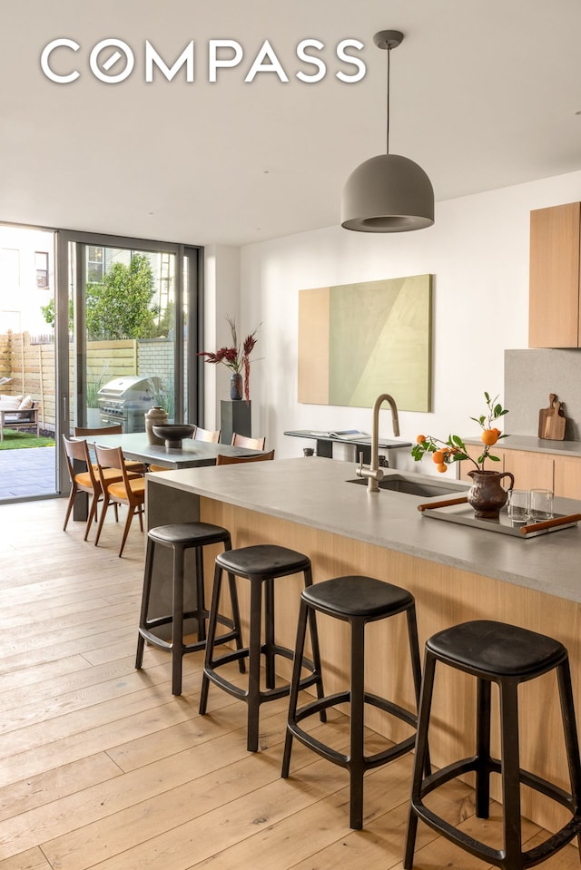 kitchen with a sink, a kitchen breakfast bar, hanging light fixtures, light wood finished floors, and a peninsula