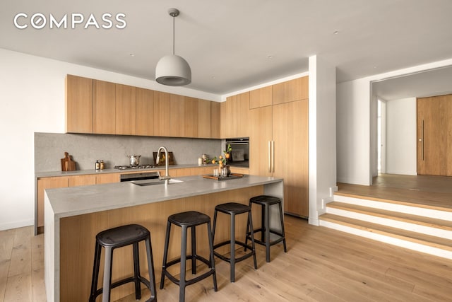 kitchen featuring a sink, modern cabinets, light wood finished floors, a breakfast bar area, and backsplash