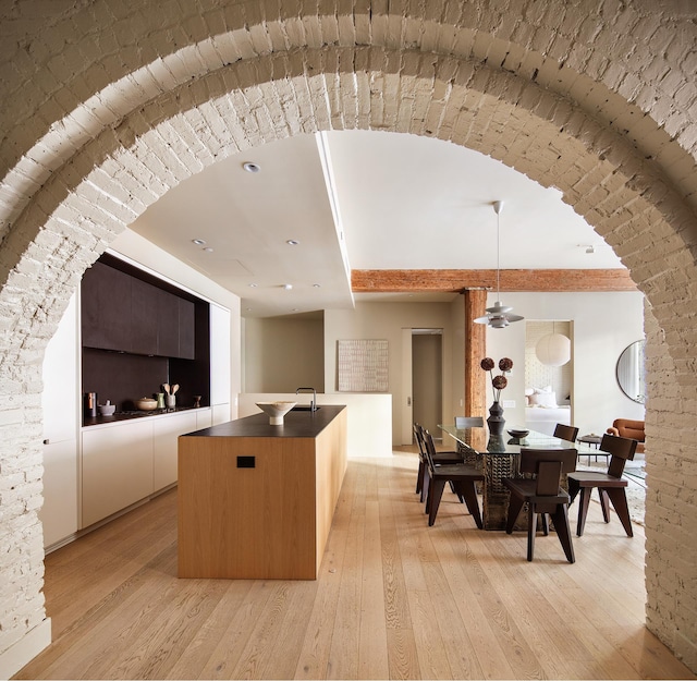 kitchen featuring a kitchen island with sink, dark countertops, light wood-style floors, modern cabinets, and hanging light fixtures