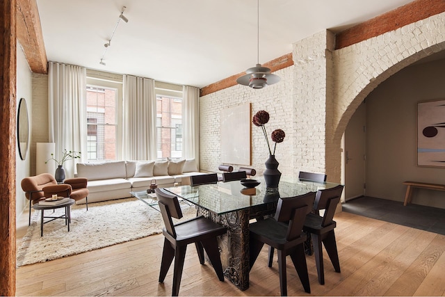 dining space with a ceiling fan, hardwood / wood-style floors, track lighting, brick wall, and arched walkways